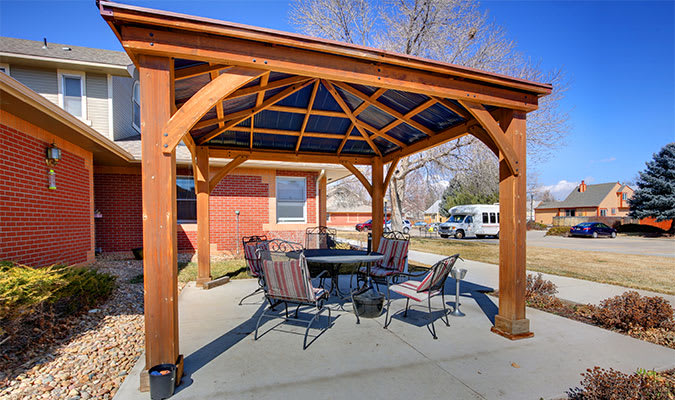 A wooden pergola with a dining set underneath, providing a shaded seating area in a backyard.
