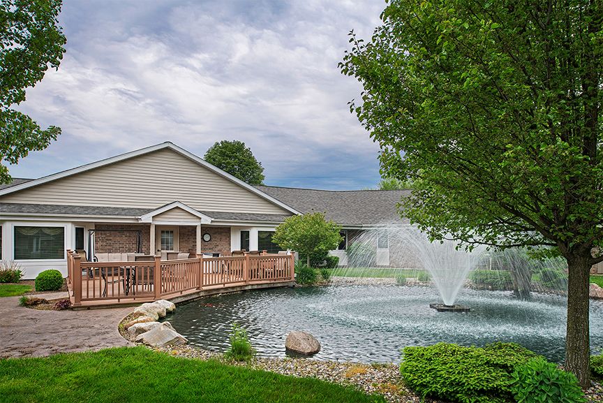 A serene view of a building with a pond and fountain surrounded by lush landscaping.