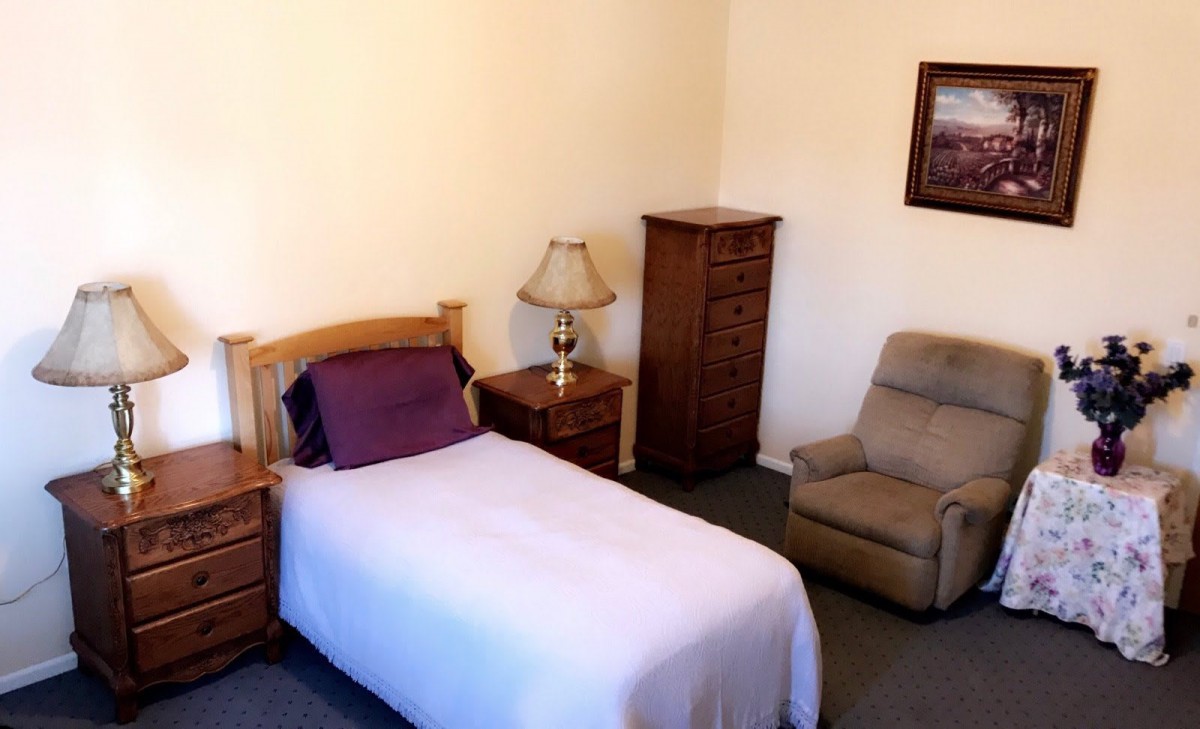 A cozy bedroom with a single bed, lamp, dresser, and comfortable chair.