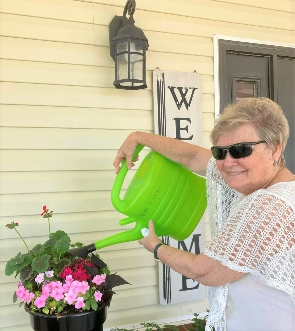 A woman smiles while watering her plants with a green watering can.