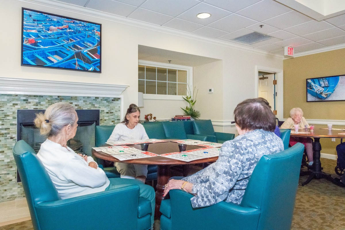 A group of elderly individuals seated in a comfortable meeting area, possibly in a retirement home, engaging in a discussion.