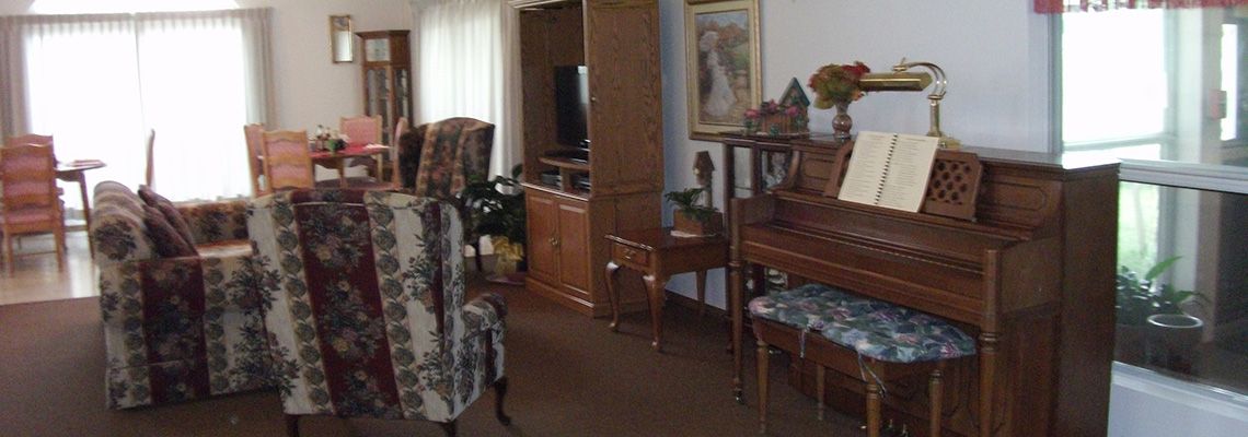A cozy living room featuring a piano, patterned chair, and a television.