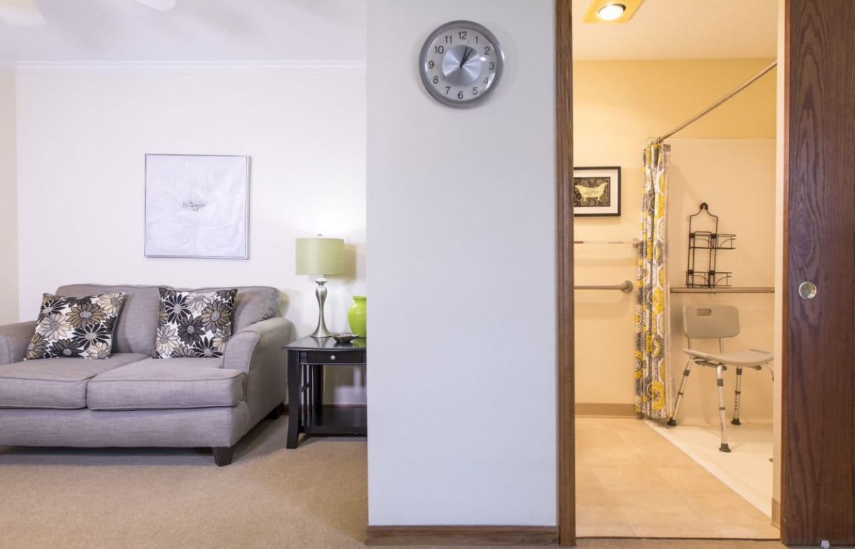 A modern interior featuring a cozy living room with a sofa and lamp on one side, and a bathroom with a shower on the other.