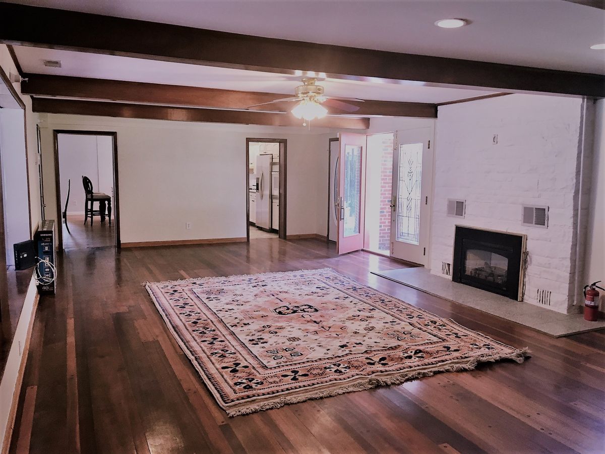Spacious living room with hardwood floors, a central area rug, and a cozy fireplace.