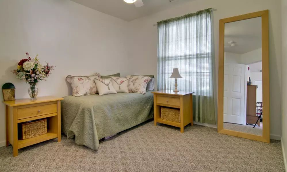 A cozy bedroom with a daybed, nightstand, and a lamp by the window.