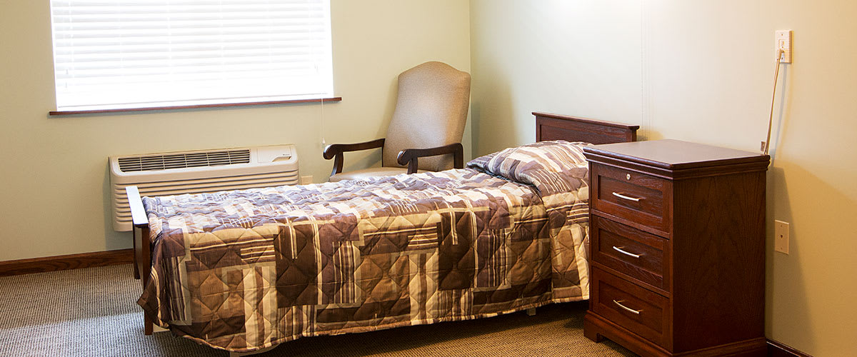A simple bedroom with a single bed, quilt, chair, and nightstand.