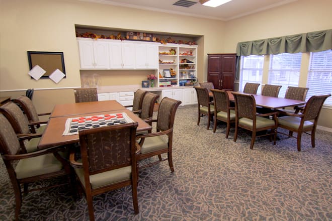 A well-organized meeting room featuring large conference tables surrounded by chairs, with a bookshelf in the background.