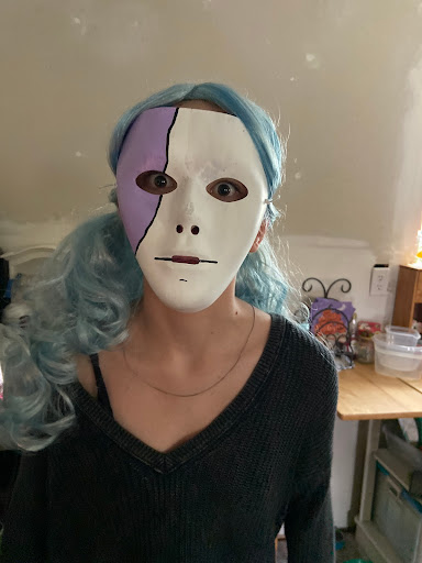 An individual with blue hair wearing a half-white, half-purple mask, creating an artistic and eerie appearance.