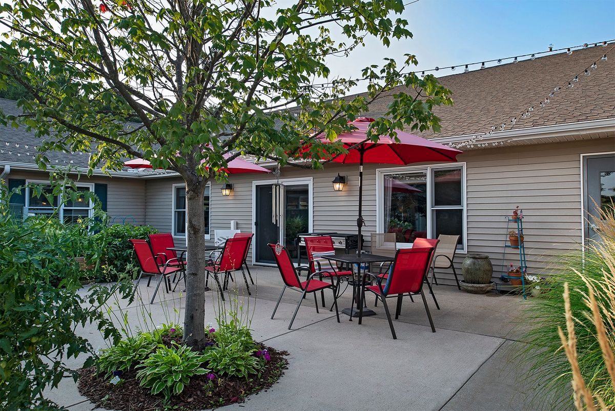 A cozy outdoor patio area with red chairs and umbrellas, surrounded by plants and trees.