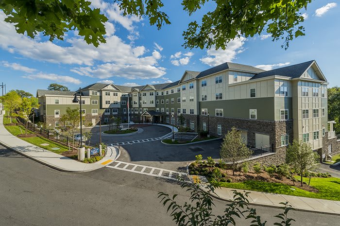 A modern apartment complex surrounded by landscaping and trees under a partly cloudy sky.