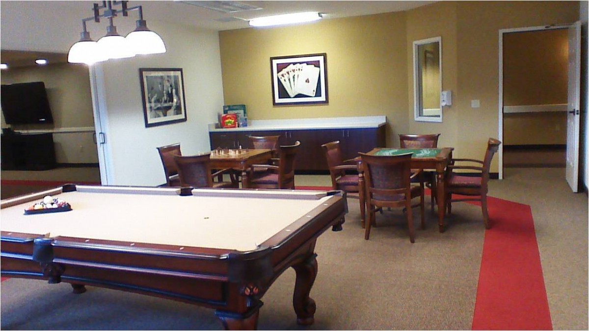 A cozy game room featuring a billiards table, chess set, and card table with wooden chairs.