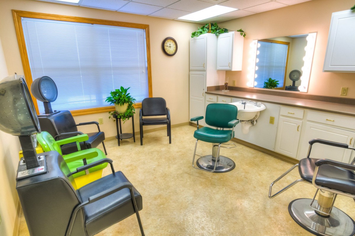 A well-lit salon interior with chairs, a mirror, and potted plants.