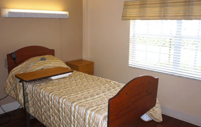 A simple bedroom with a single bed, nightstand, and window.