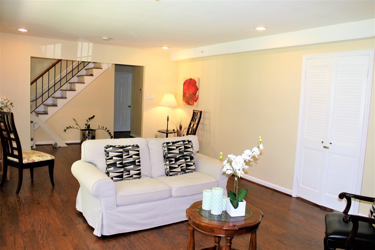 A modern living room with a white sofa, decorative pillows, and a side table with plants.