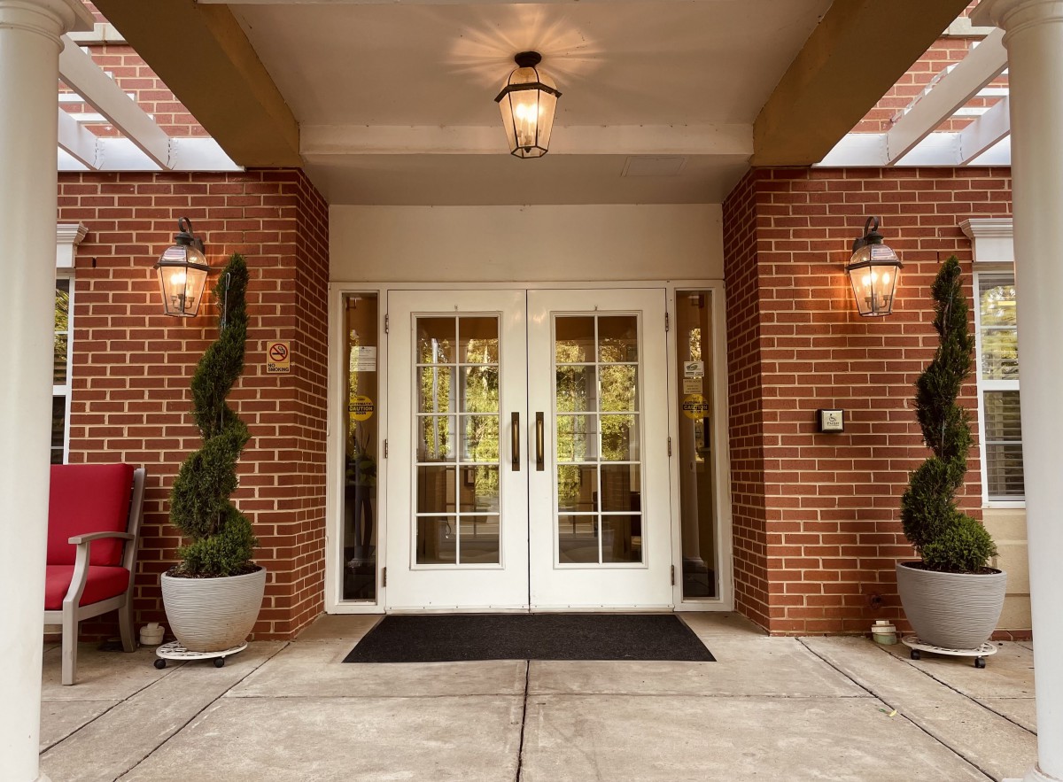 A welcoming entrance with double glass doors set in a brick building, adorned with decorative plants and warm lighting.