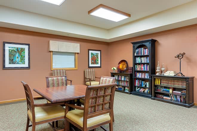 A cozy meeting room featuring a table with chairs, a bookshelf filled with books, and artwork on the wall.