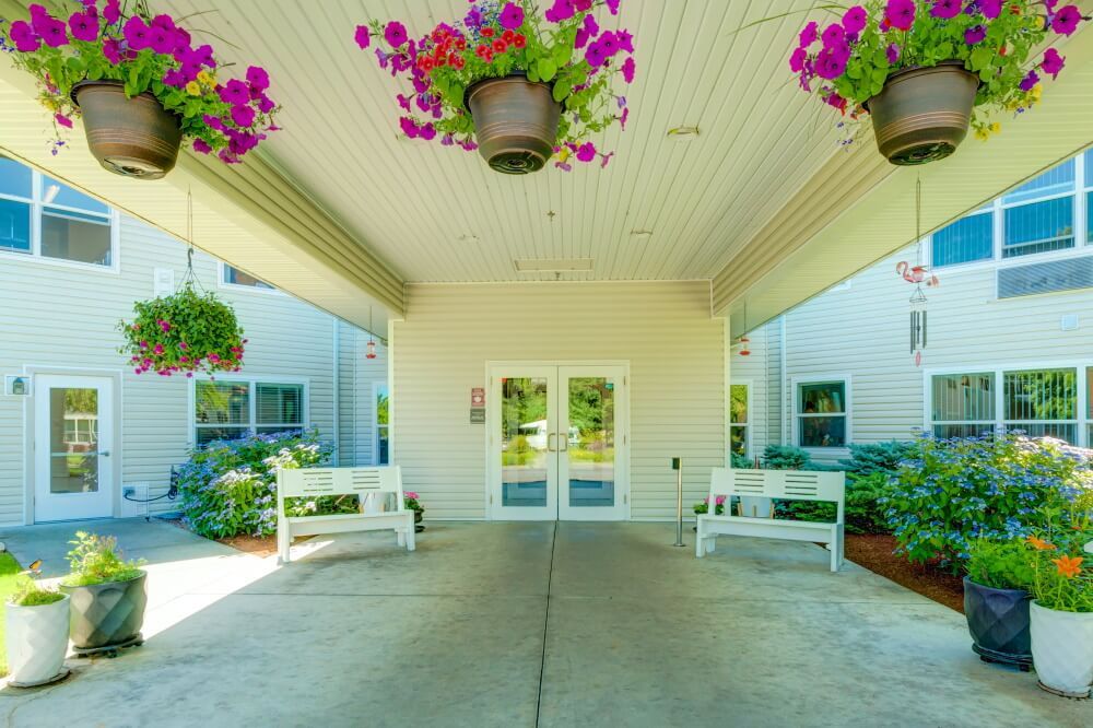 Covered entrance of a building with benches and hanging flower pots.