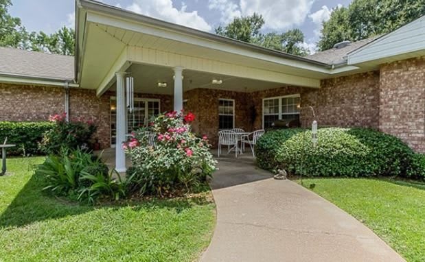 A charming brick house with a covered porch and landscaped garden area featuring blooming flowers.