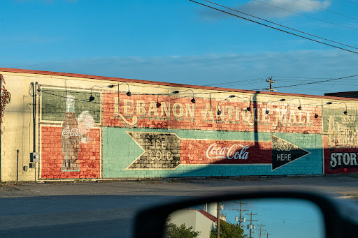 A weathered mural featuring vintage advertisements, including Coca-Cola, on the side of a building in Lebanon.