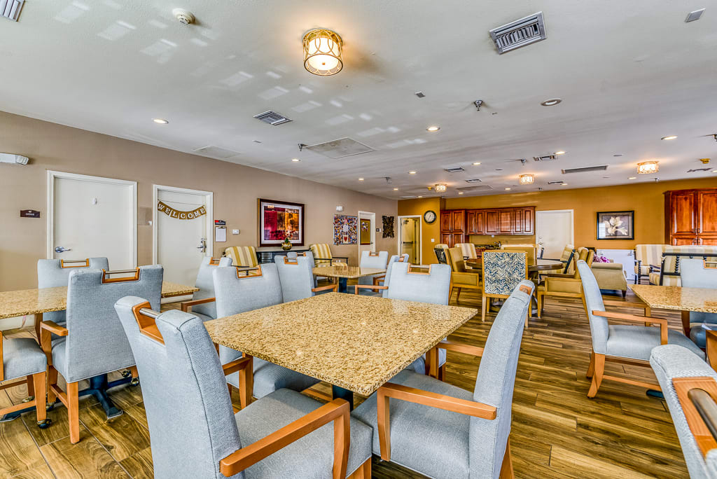 A modern dining room with multiple tables and chairs, featuring wooden floors and ceiling lights.