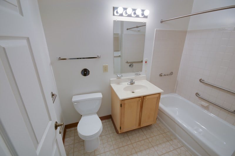 A clean and simple bathroom with a toilet, sink, mirror, and bathtub.