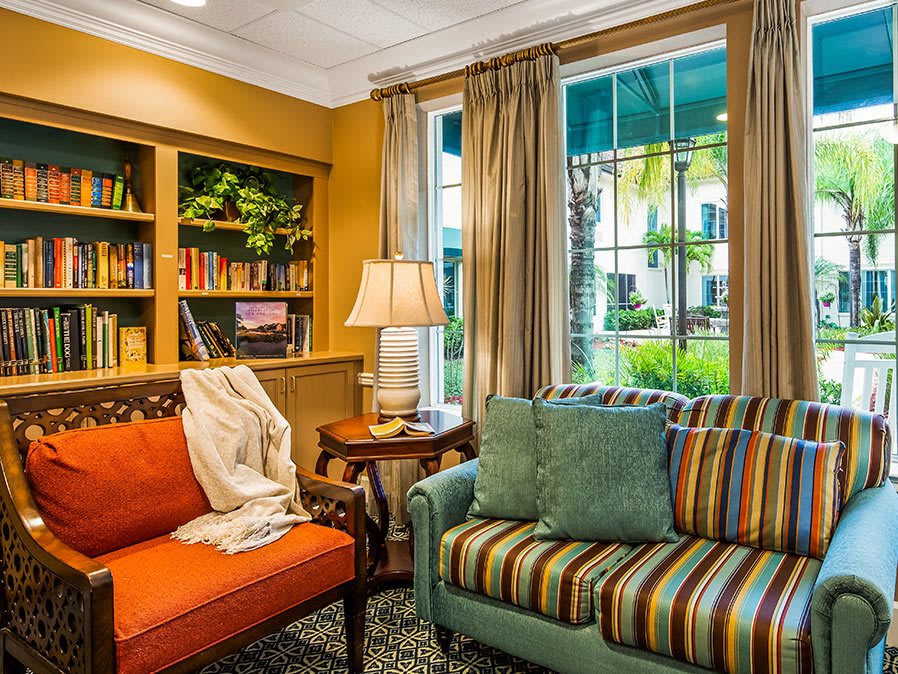 A cozy living room with colorful sofas, a bookshelf, and a window view.