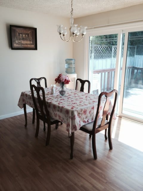 A cozy dining area with a table set for four, adorned with a floral tablecloth and centerpiece, illuminated by a chandelier, and adjacent to large sliding doors.