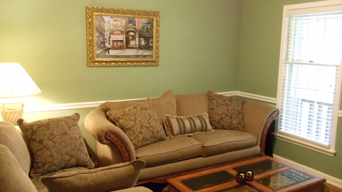 A cozy living room with a beige sofa, patterned cushions, and wall art on green-painted walls.