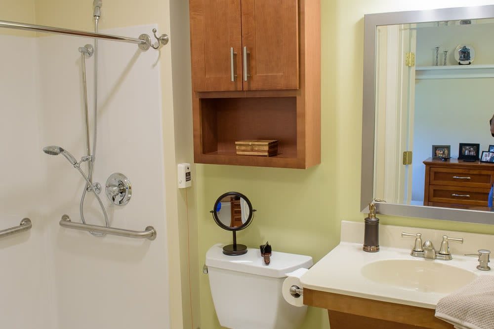 A clean and organized bathroom featuring a shower, toilet, sink with a mirror, and wooden cabinets.