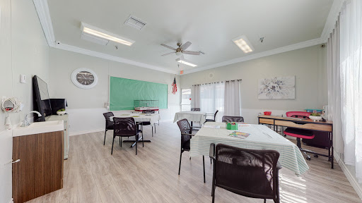 A spacious and well-lit classroom setup, featuring a green chalkboard and arranged tables and chairs.