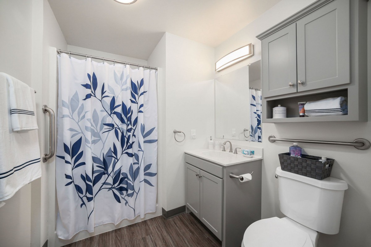 A modern bathroom featuring a blue and white leafy shower curtain, a sink with a mirror, and storage cabinets.