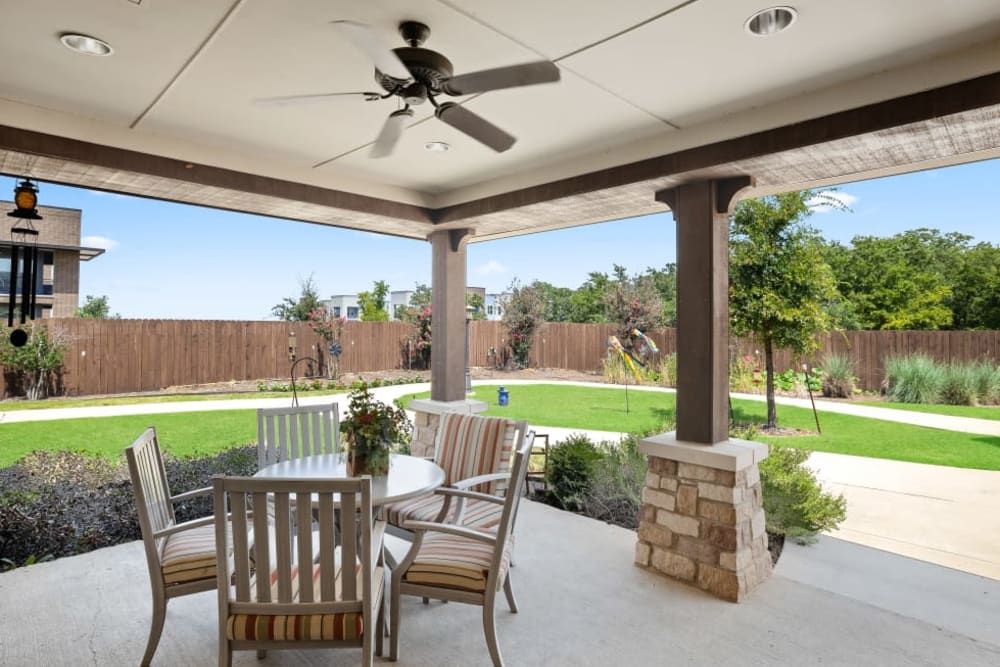 A serene backyard patio with seating area and ceiling fan overlooking a well-maintained garden and lawn.