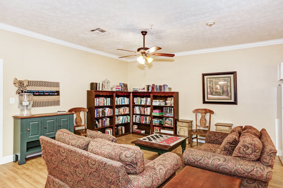 A cozy living room with bookshelves, seating area, and a ceiling fan.