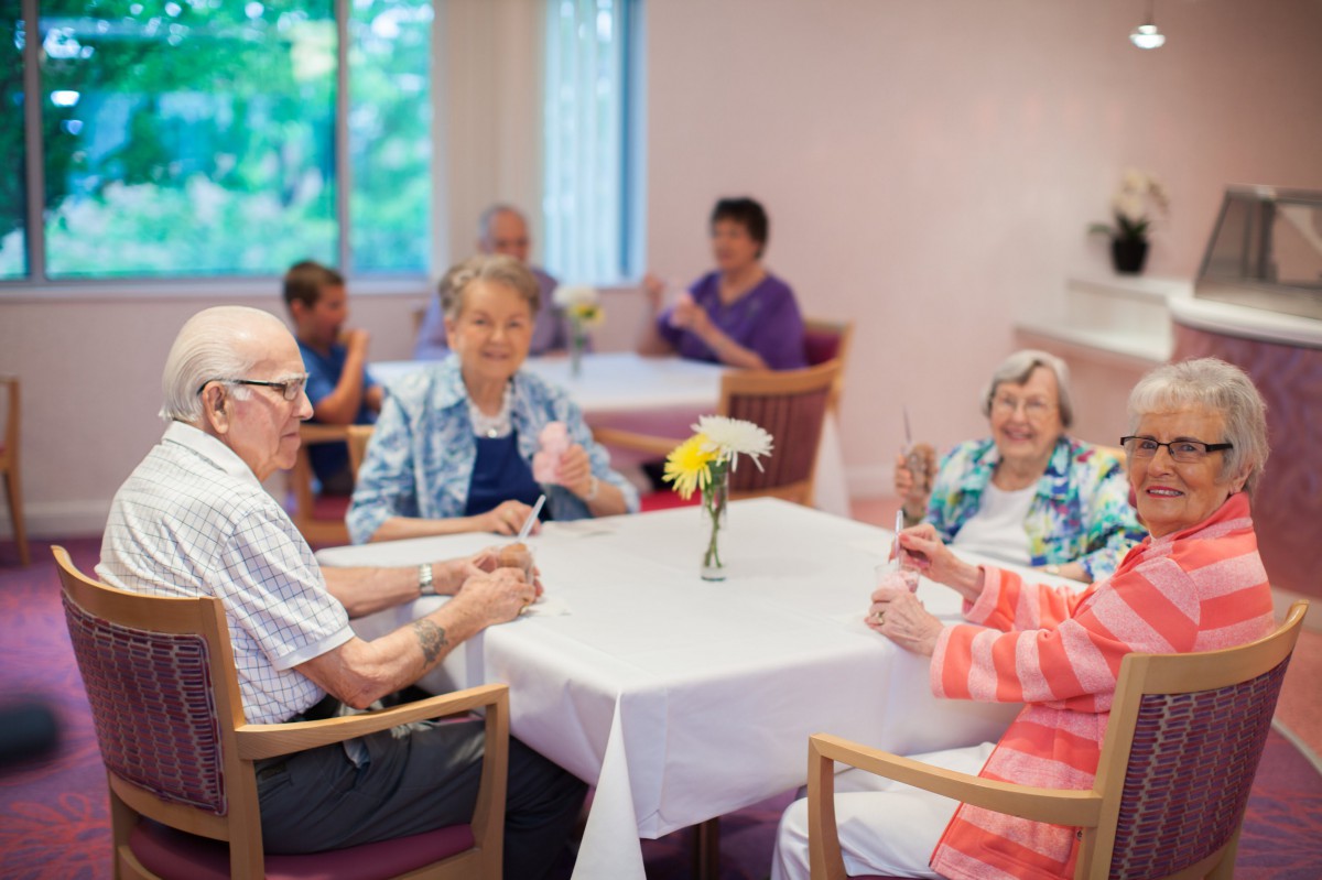 A group of elderly people socializing around a table with flowers in a community setting.