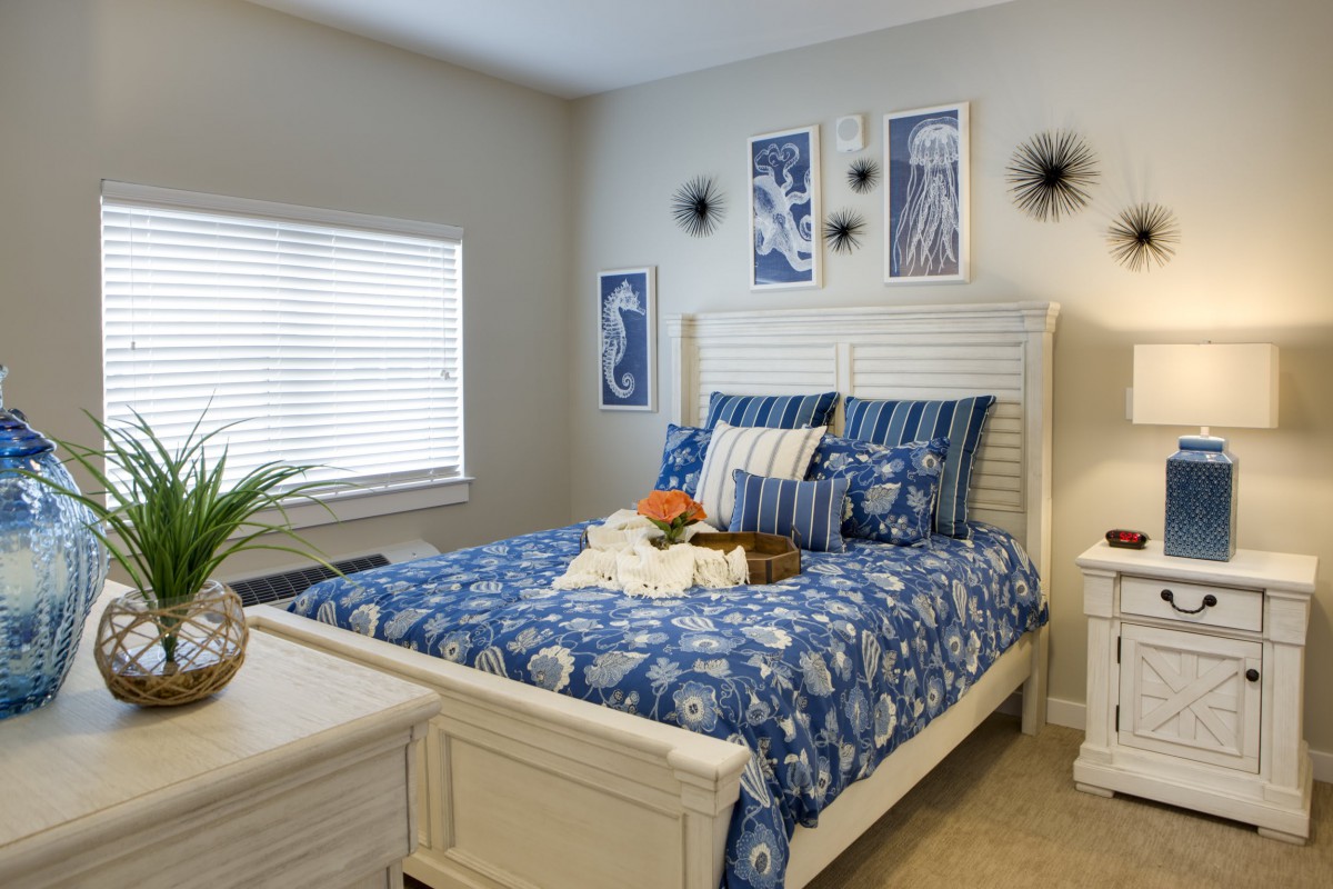 A cozy bedroom with a blue and white theme, featuring a neatly made bed with matching bedding and wall art.