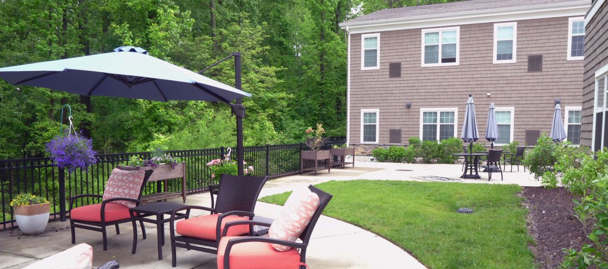 A peaceful backyard patio setup with outdoor seating, umbrella, and lush greenery.