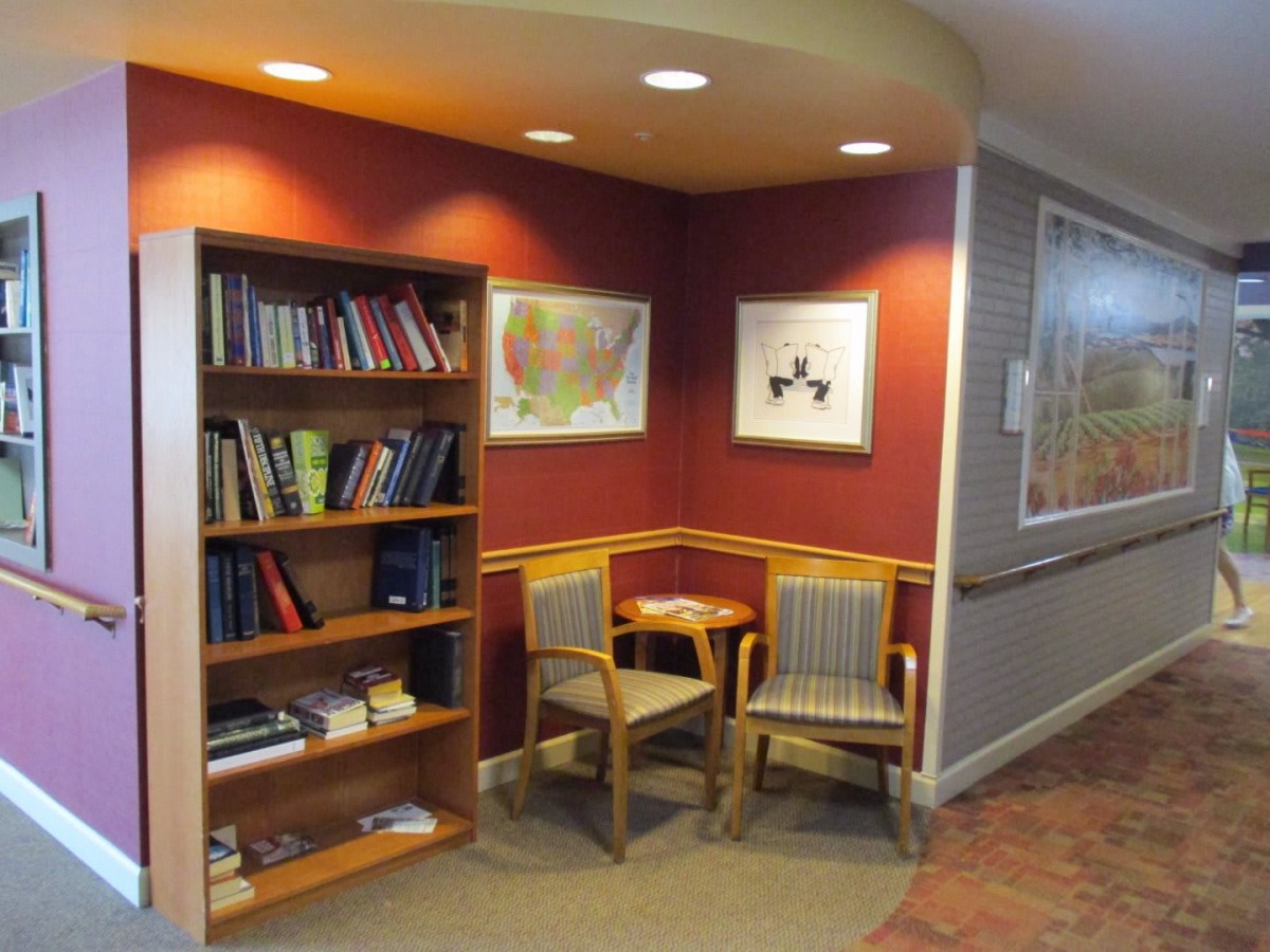 A cozy reading nook with a bookshelf, armchairs, and a small table, adorned with artwork on the walls.