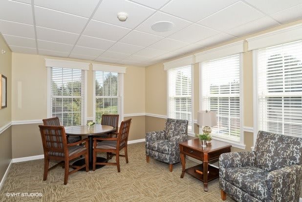 A cozy living room with ample natural light, featuring a seating area and large windows.