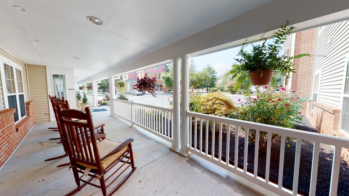 A cozy porch with a rocking chair and hanging plants, overlooking a garden.