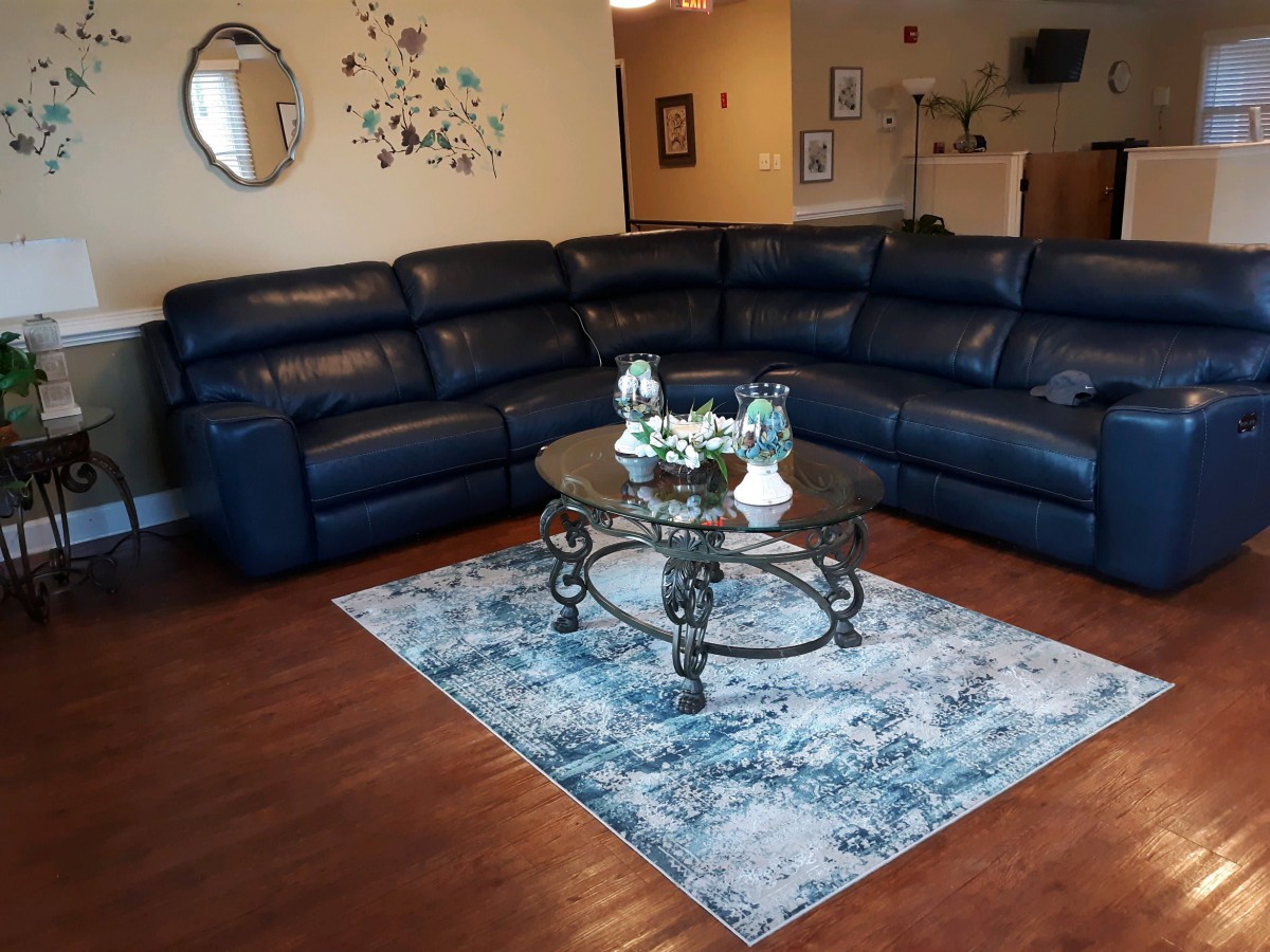 A cozy living room with a blue sectional sofa, a glass coffee table, and a patterned area rug.