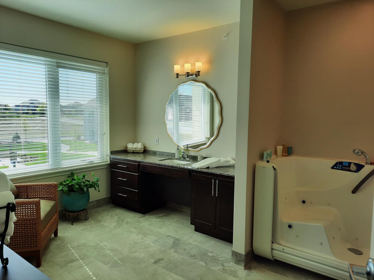 A modern bathroom featuring a vanity with an oval mirror, a window for natural light, and a cozy bathtub.
