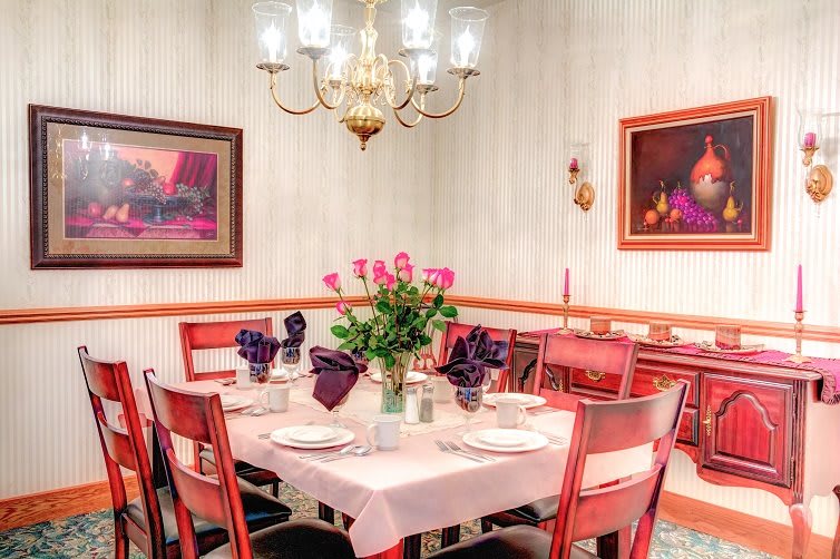 A cozy dining room with a beautifully set table and floral centerpiece under a warm chandelier light.