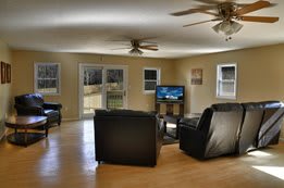 A spacious living room with black leather sofas, a TV, and ceiling fans.