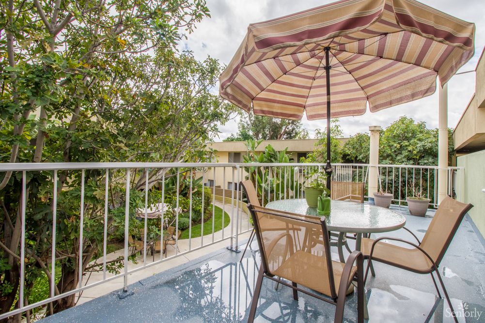 A serene balcony with a patio set, featuring an umbrella and a view of lush greenery.