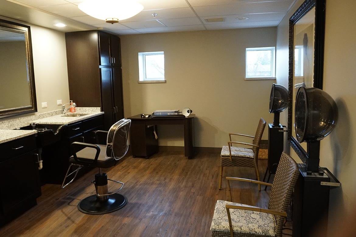 An interior view of a hair salon with a styling chair, mirror, and workspace.