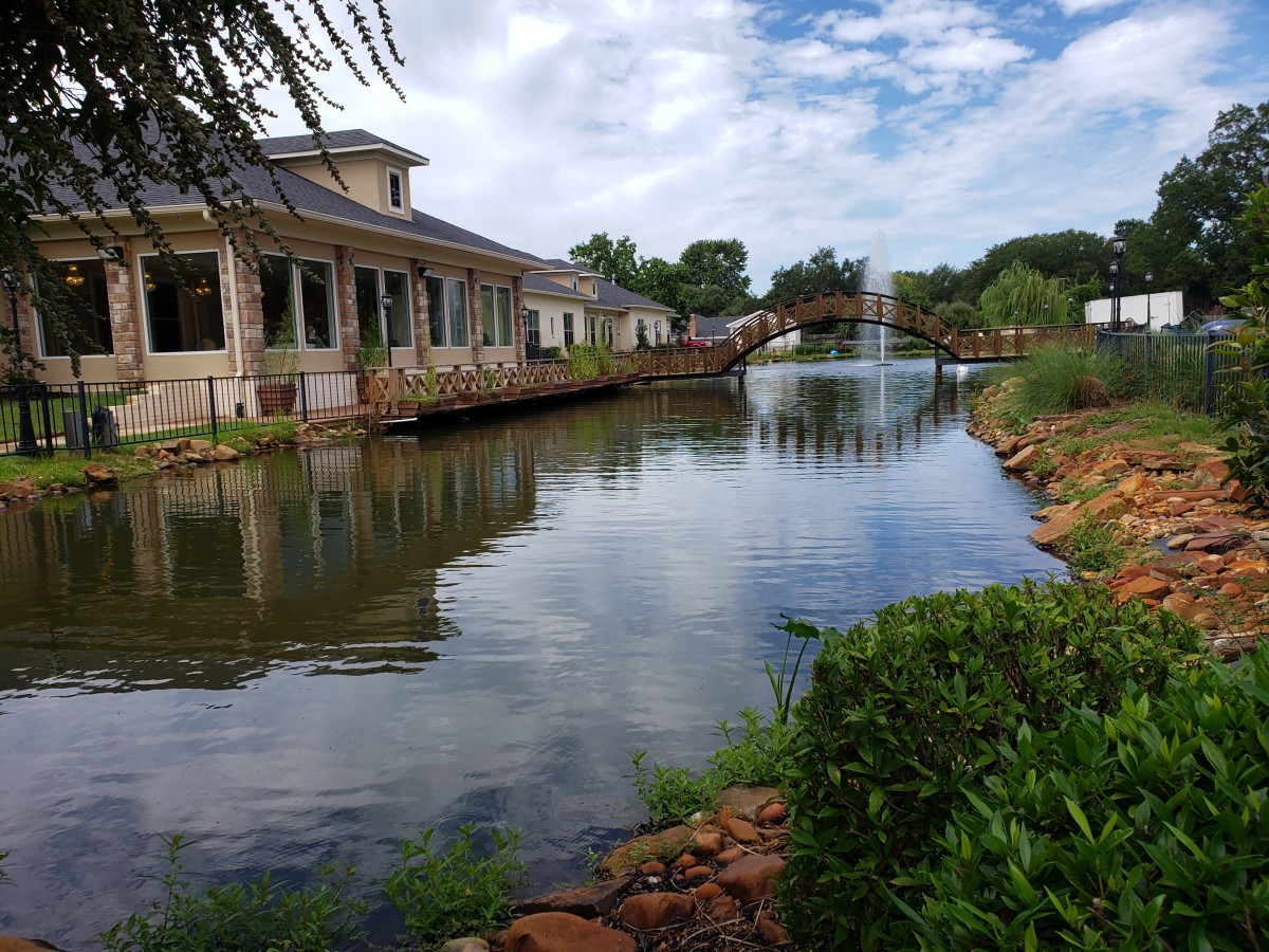A serene view of a bridge and buildings alongside a lake under a cloudy sky.