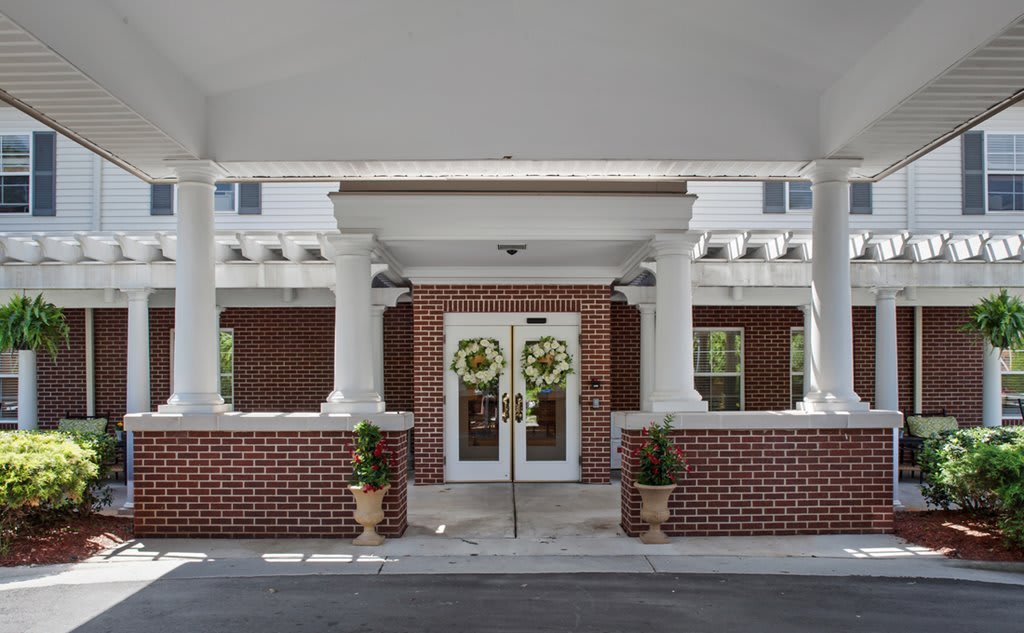 Front entrance of a building featuring double doors with wreaths, columns, and brick walls.
