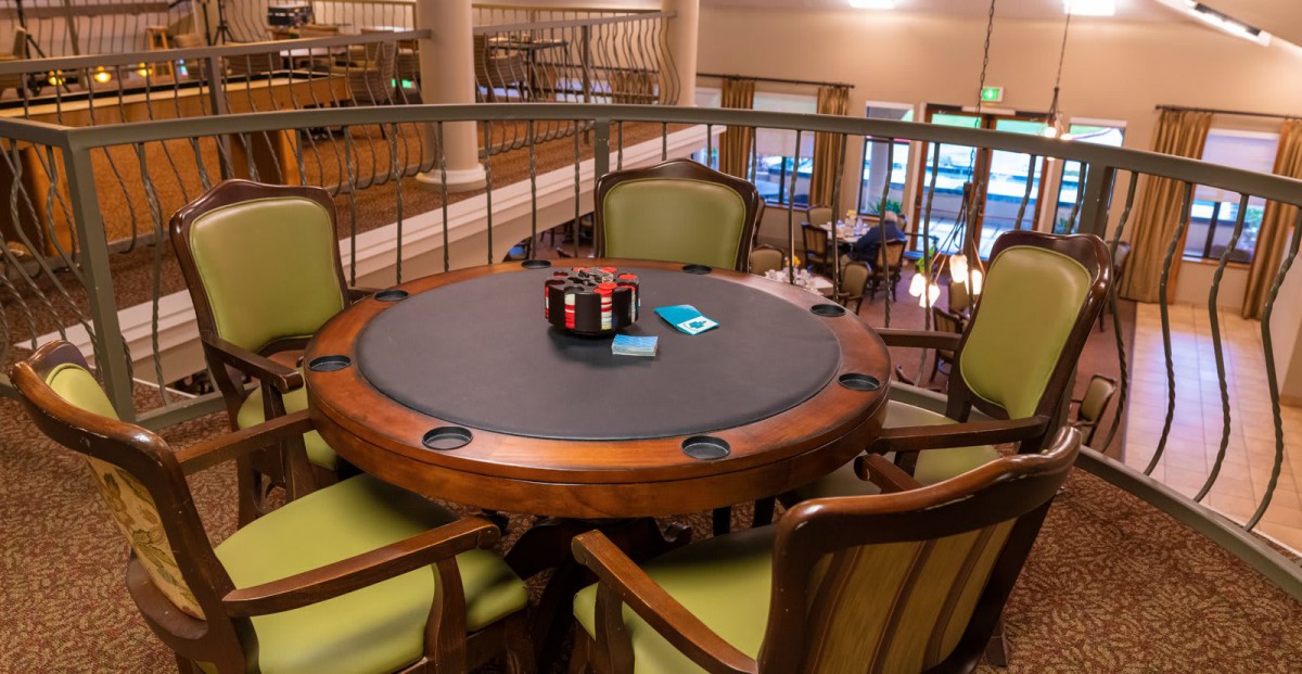 A poker table set up with cards and chips, surrounded by chairs in a game room.