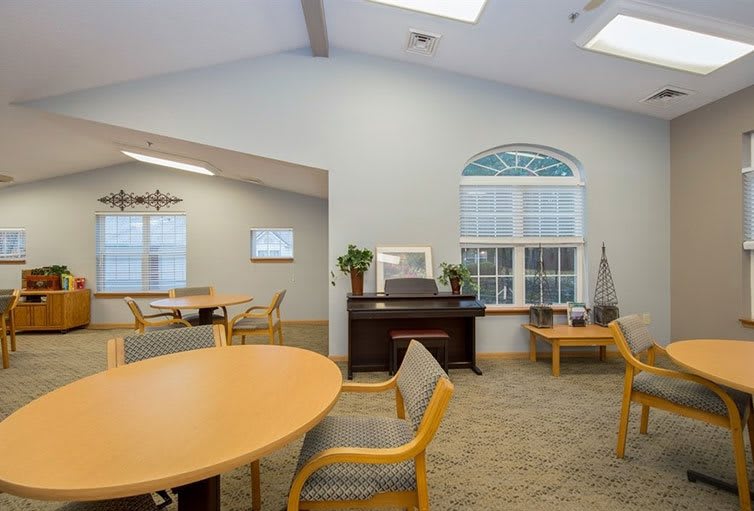A cozy lounge area with round tables, chairs, a piano, and large windows.