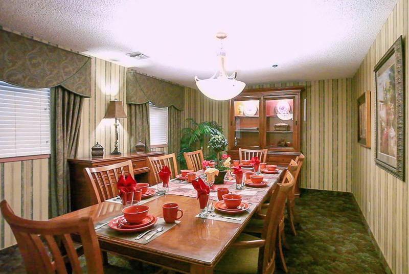 A well-decorated dining room with a large wooden table set for a meal, featuring red dinnerware and a central chandelier.